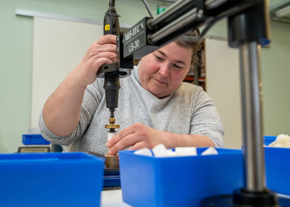 Eine Frau mit Behinderung bedient eine Maschine zur Montage von Metallteilen
