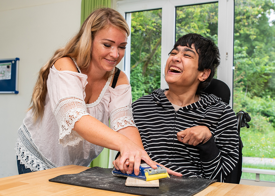 Frau mit Behinderung und ihre Betreuerin lachen gemeinsam bei der Arbeit