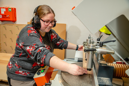 Frau mit Behinderung arbeitet an einer Holzmaschine 